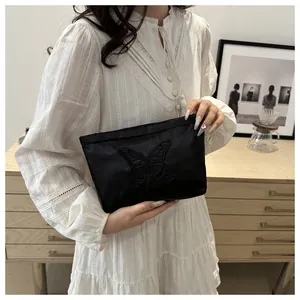 Detail of elegant black satin clutch bag with intricate butterfly embroidery and zipper