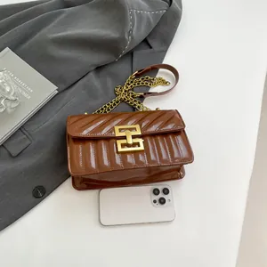 Brown quilted crossbody bag with gold chain strap and metal lock shown with phone for scale