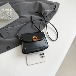 Retro black leather saddle bag with gold arch buckle on grey suit background