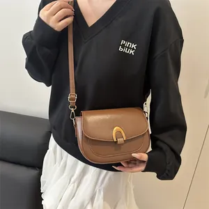 Sacoche marron en similicuir avec boucle fer à cheval dorée portée à l'épaule