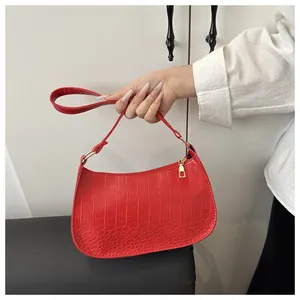 Detail of red crocodile textured crescent bag with gold zipper held by a model