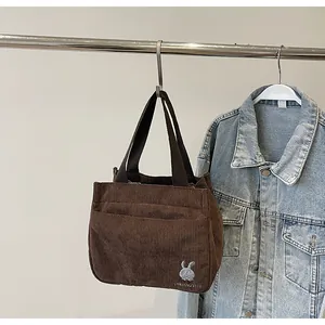 Détail de broderie lapin blanc sur un sac à main en velours côtelé marron foncé