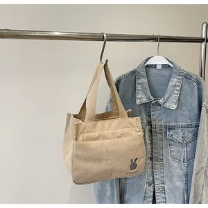 Gros plan d'un sac cabas en velours côtelé beige avec broderie lapin sur crochet