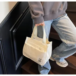 Gros plan d'un sac cabas en velours côtelé beige avec broderie lapin et texture