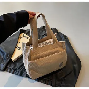 Détail du cabas en velours côtelé beige avec lapin brodé et larges poignées sur cuir noir