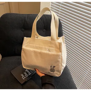 Détail de la broderie de lapin gris et du nom de marque sur un sac cabas en velours
