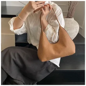 Close-up of a brown woven crescent shoulder bag on a model wearing a white shirt