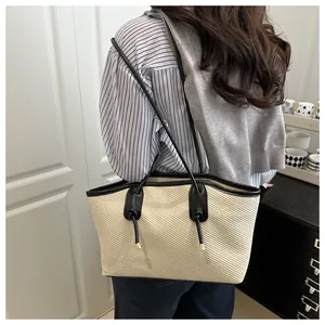 Detail view of beige woven tote bag with black rope handles and gold metallic tips