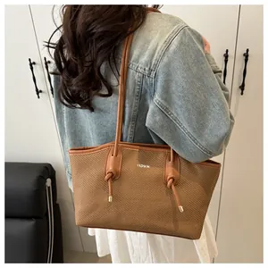 Detail of a brown woven tote bag with FASHION lettering and slim knotted leather straps