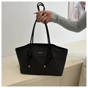 Detail of black tote bag with woven texture, silver FASHION logo and knotted handles