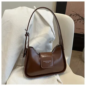 Detail of dark brown patent leather shoulder bag with buckle strap and gold text logo