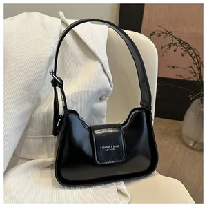 Detail of black polished leather underarm bag with adjustable strap and white text logo
