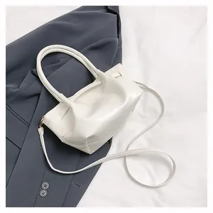 Detail of minimalist cream leather bucket bag with top handles and adjustable strap