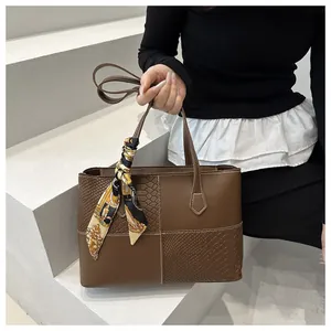 Detailed view of brown tote bag featuring textured leather panels and silk scarf handle wrap