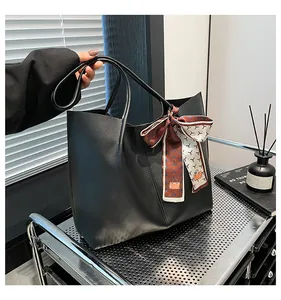 Detail of a black matte leather tote bag with a geometric printed silk scarf on the handle