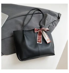 Detail of black PU leather tote bag with elegant silk scarf and sleek shoulder straps