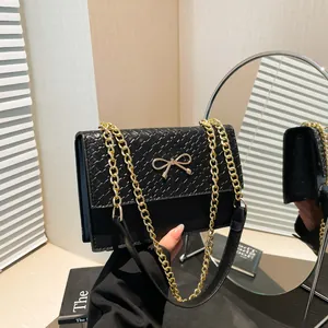 Elegant black crossbody bag with woven texture and a gold metal bow accent on the front