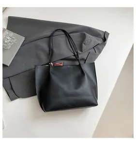 Detailed top view of a minimalist black matte PU leather tote bag on a grey blazer suit