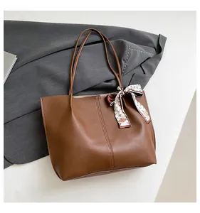 Macro view of brown leather tote bag with decorative silk scarf and vertical stitching