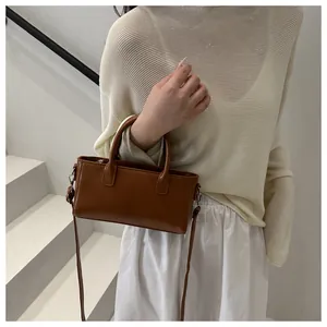 Piccola borsa quadrata in pelle marrone con doppi manici e logo indossata da modella