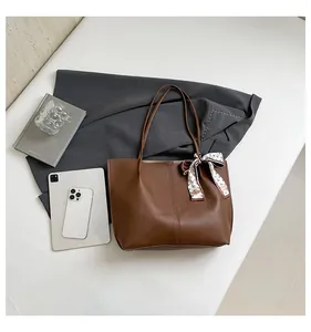 Flat lay of brown leather tote bag with printed silk scarf and office accessories