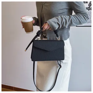 Détail du sac carré noir texturé avec poignée tressée et finitions métalliques dorées