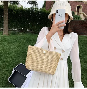 Detail of hand-woven straw tote bag featuring white handles and round button closure
