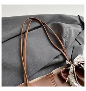 Detailed view of brown leather tote bag with elegant geometric scarf on grey blazer background