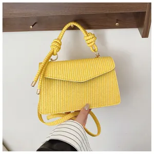 Détail d'un sac à main carré tissé jaune avec poignée nouée et rabat enveloppe