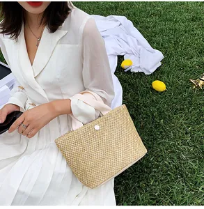 Detail of hand-woven straw tote bag with fabric handles and button closure on green grass