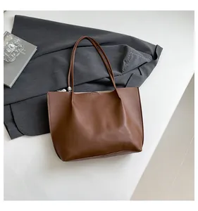 Flat lay of brown matte leather tote bag with long straps on a white desk with props