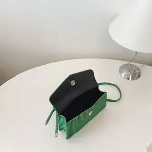 Petit sac carré tressé vert avec boucle magnétique dorée sur un fond blanc épuré