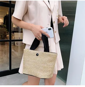 Detailed macro view of woven straw tote bag with black strap and decorative button