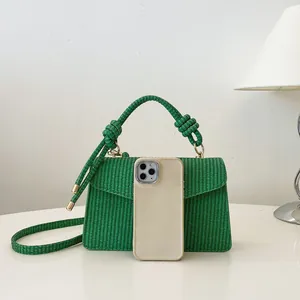 Sac à main tissé vert avec poignée nouée et bandoulière à côté d'un téléphone