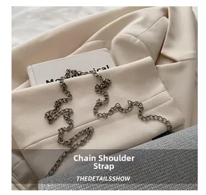 Close-up of gunmetal chain strap on a silver glitter crossbody bag over a beige blazer