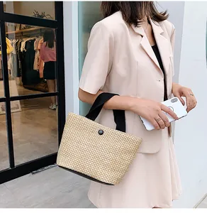 Detailed close-up of woven straw handbag with black handles and button closure