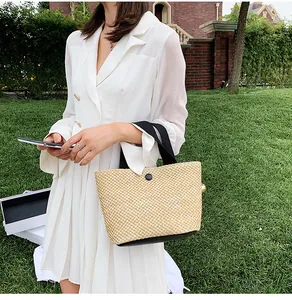 Detail of woven straw handbag with black handles and buckle on green grass background