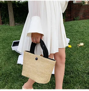 Detail of beige straw handbag with black button accent and fabric handles on grass