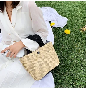 Close-up of summer woven straw handbag with black straps on green grass and white tablecloth