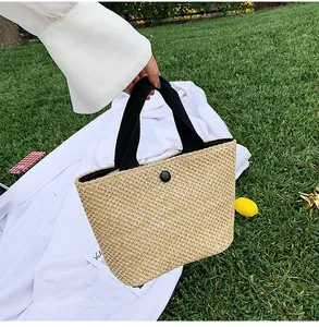 Close-up of woven straw handbag featuring black fabric handles and a round button closure