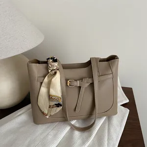 Minimalist khaki leather tote bag with silk scarf and metal buckle on wooden table