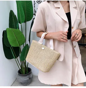 Detailed close-up of handmade straw woven handbag with white canvas straps and button detail