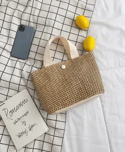 Detail view of woven straw tote bag with fabric handles and button on checkered background