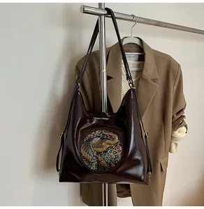 Detail of dark brown leather tote featuring a golden elephant relief and dual straps