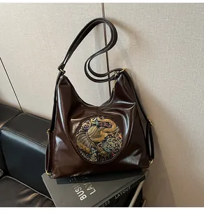 Detail of a brown glossy leather tote bag featuring a vintage golden elephant relief
