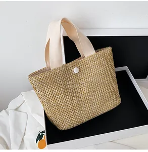 Detail of hand-woven beige straw handbag with canvas handles and round button closure