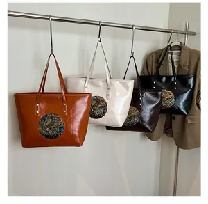Close-up of four embossed tote bags in caramel, cream, coffee, and black displayed on a rack