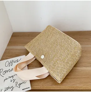 Detailed view of woven straw tote bag with cream cotton handles and a white button closure