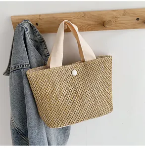 Detailed close-up of woven straw handbag with sturdy cream handles and white snap button