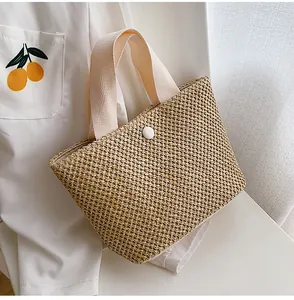 Close-up of woven straw handbag featuring white ribbon handles and a central round button